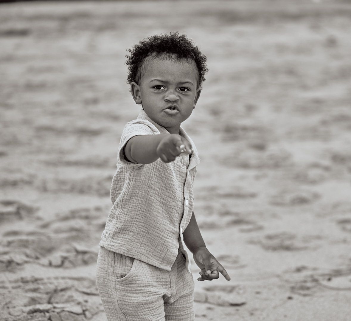 Expressive toddler pointing while standing on beach in black and white photograph.