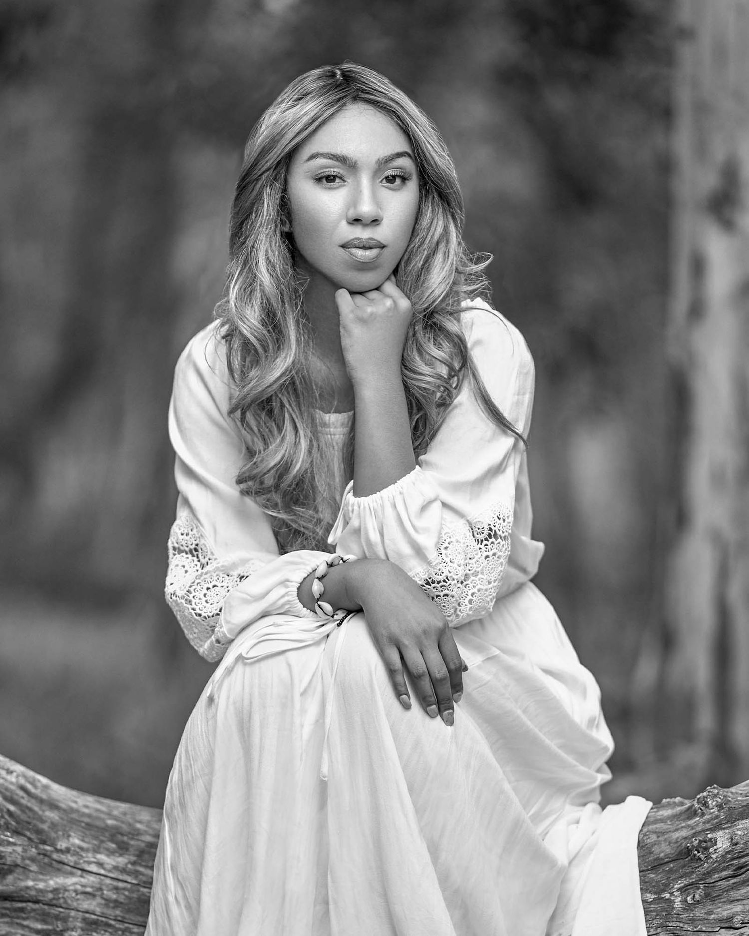 Artistic black and white portrait of a person in a white embroidered dress outdoors.