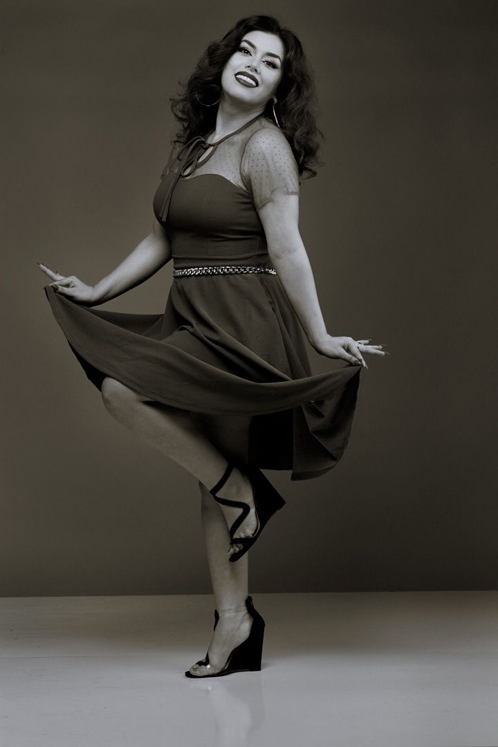 Vintage-style portrait of a person in a flared dress striking a playful dance pose.