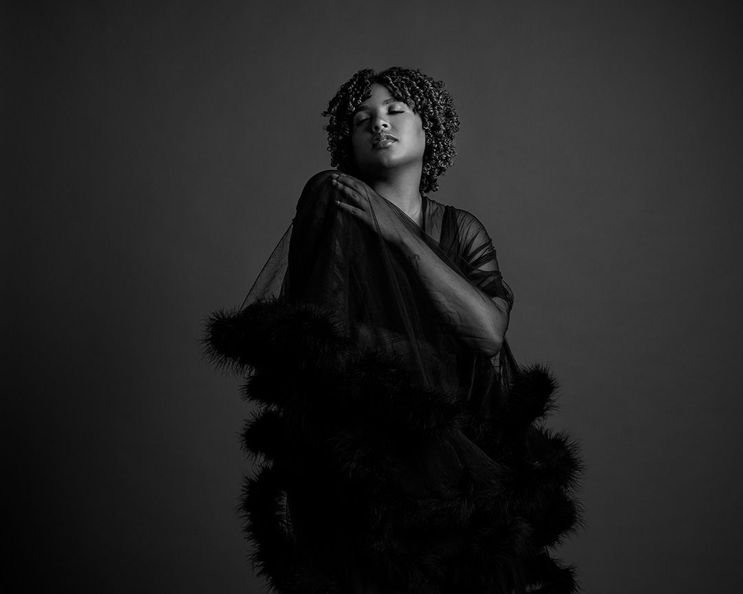 Dramatic black and white portrait featuring a person draped in dark feathered fabric.