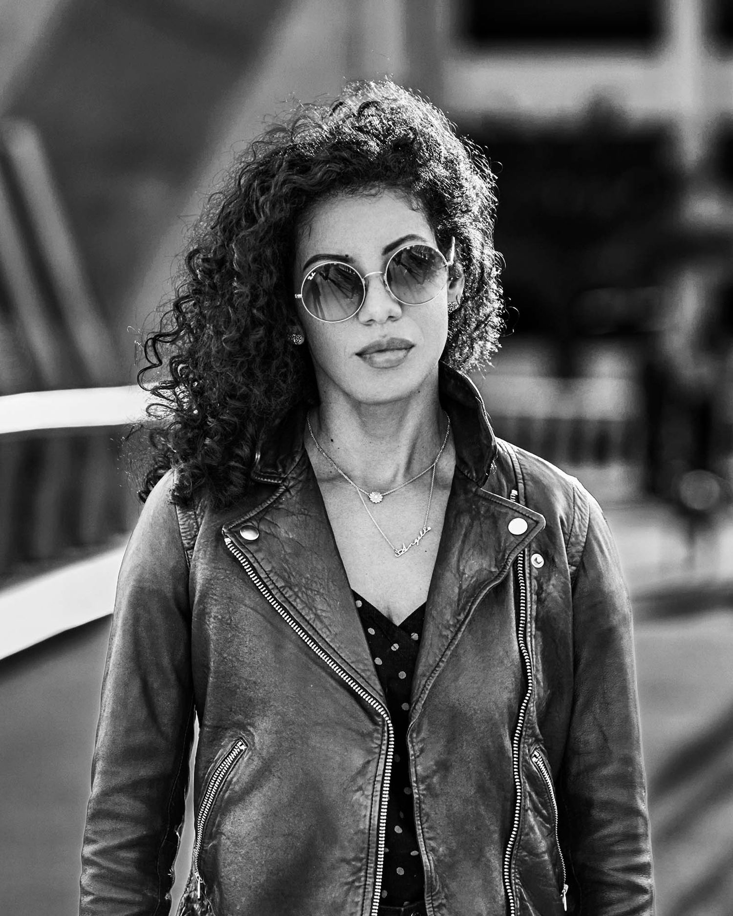 Urban portrait of someone with curly hair wearing a leather jacket and sunglasses.