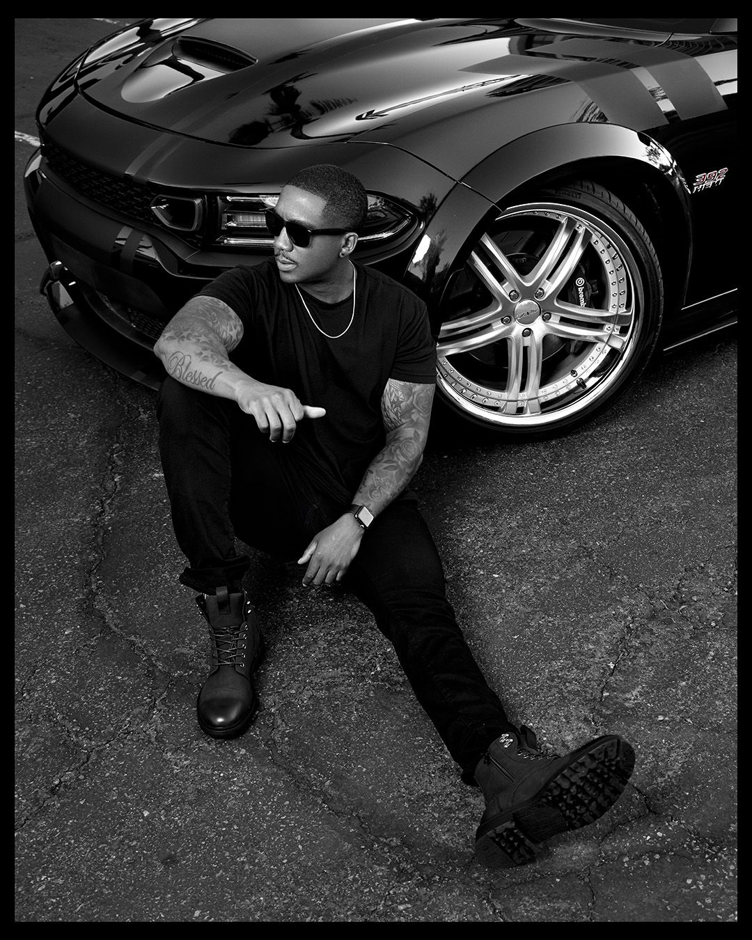 Urban fashion portrait showing someone crouching next to a luxury sports car with chrome wheels.