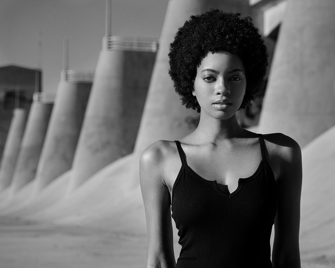 Black and white portrait of a person in a black tank top against industrial concrete columns.