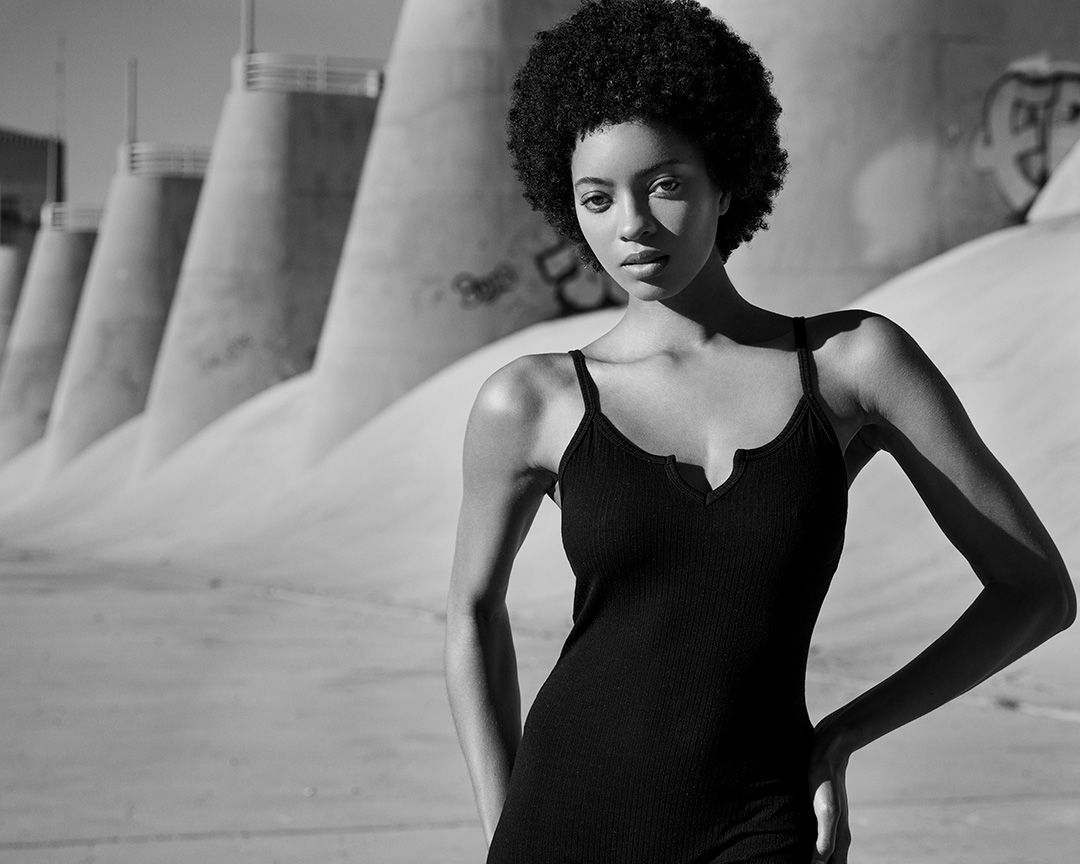 Striking black and white portrait of a person in a black dress against industrial architecture.