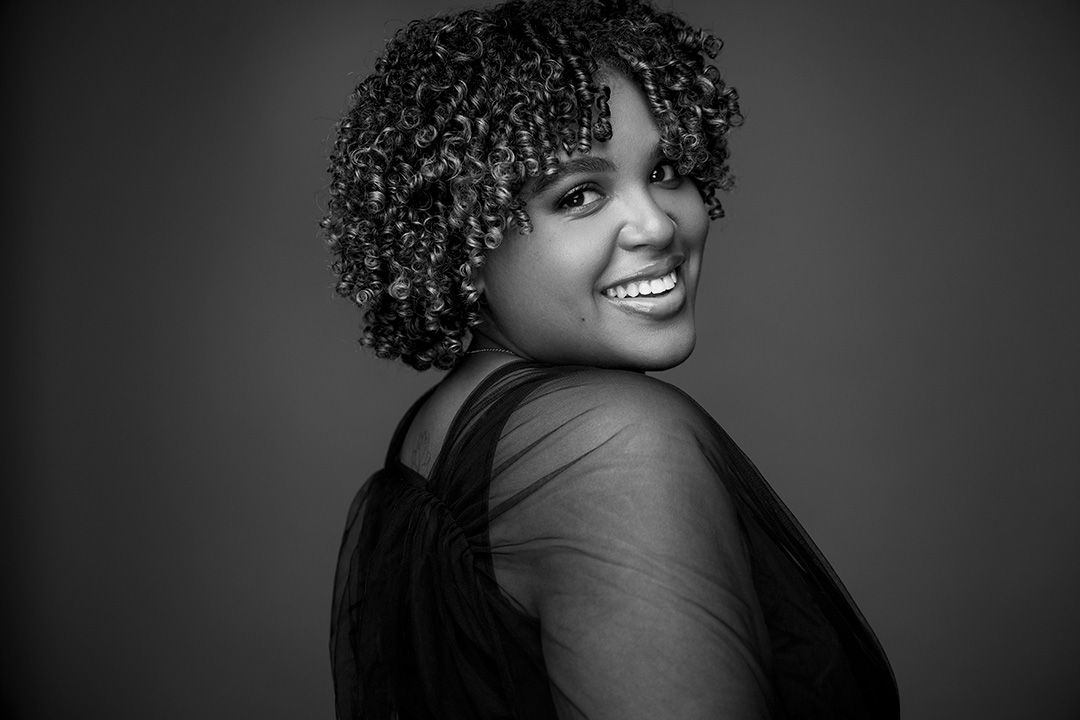 Black and white studio portrait showing a joyful expression against a dark background.