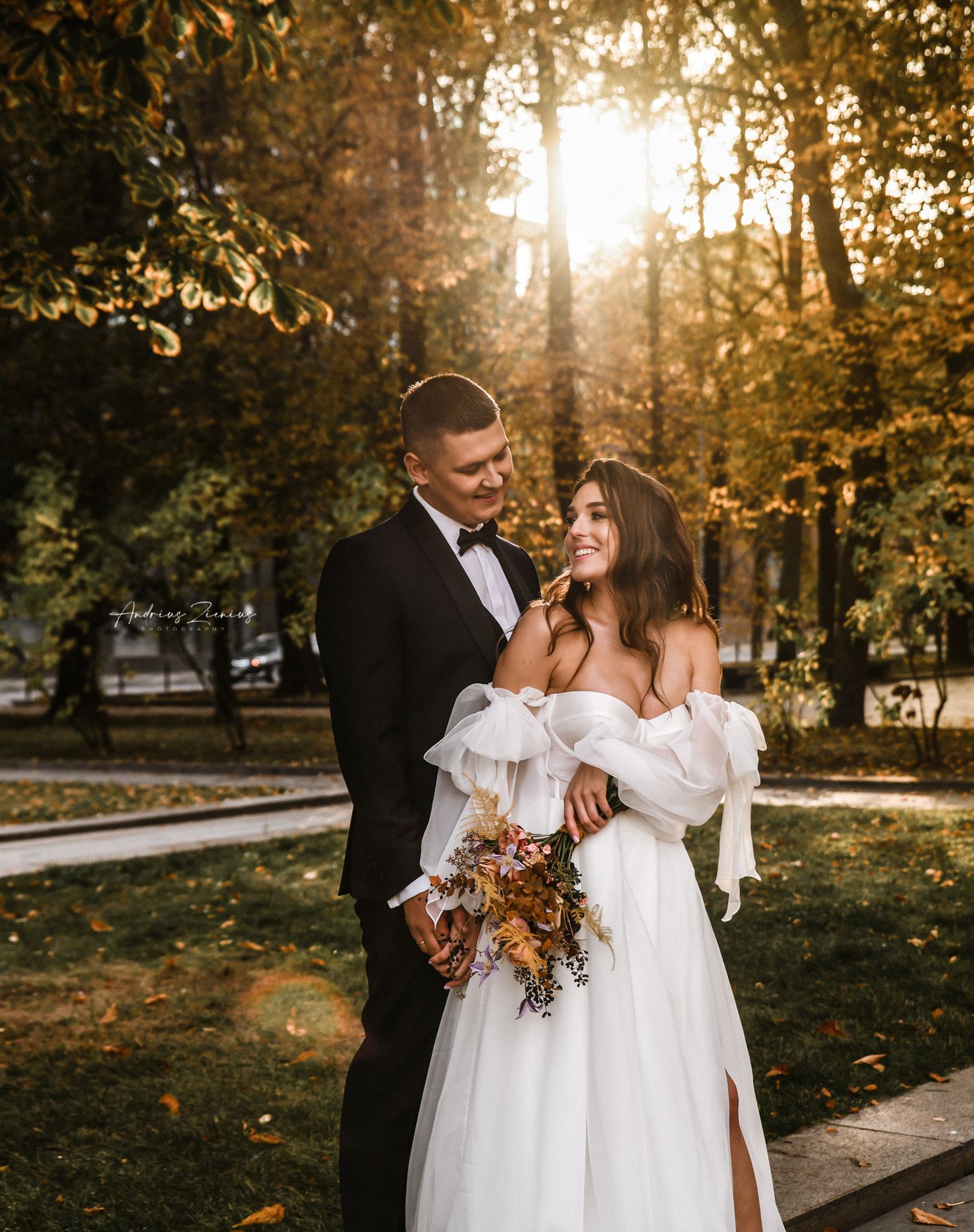 Romantic sunset wedding portrait in an autumn park with golden light filtering through trees.