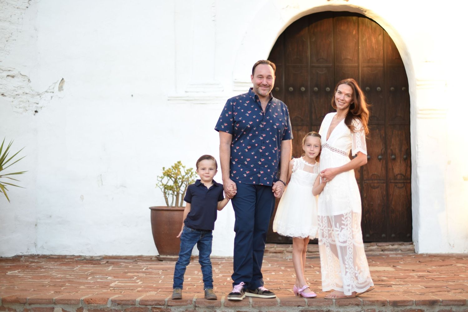 Family portrait in front of rustic wooden door and white stucco wall.