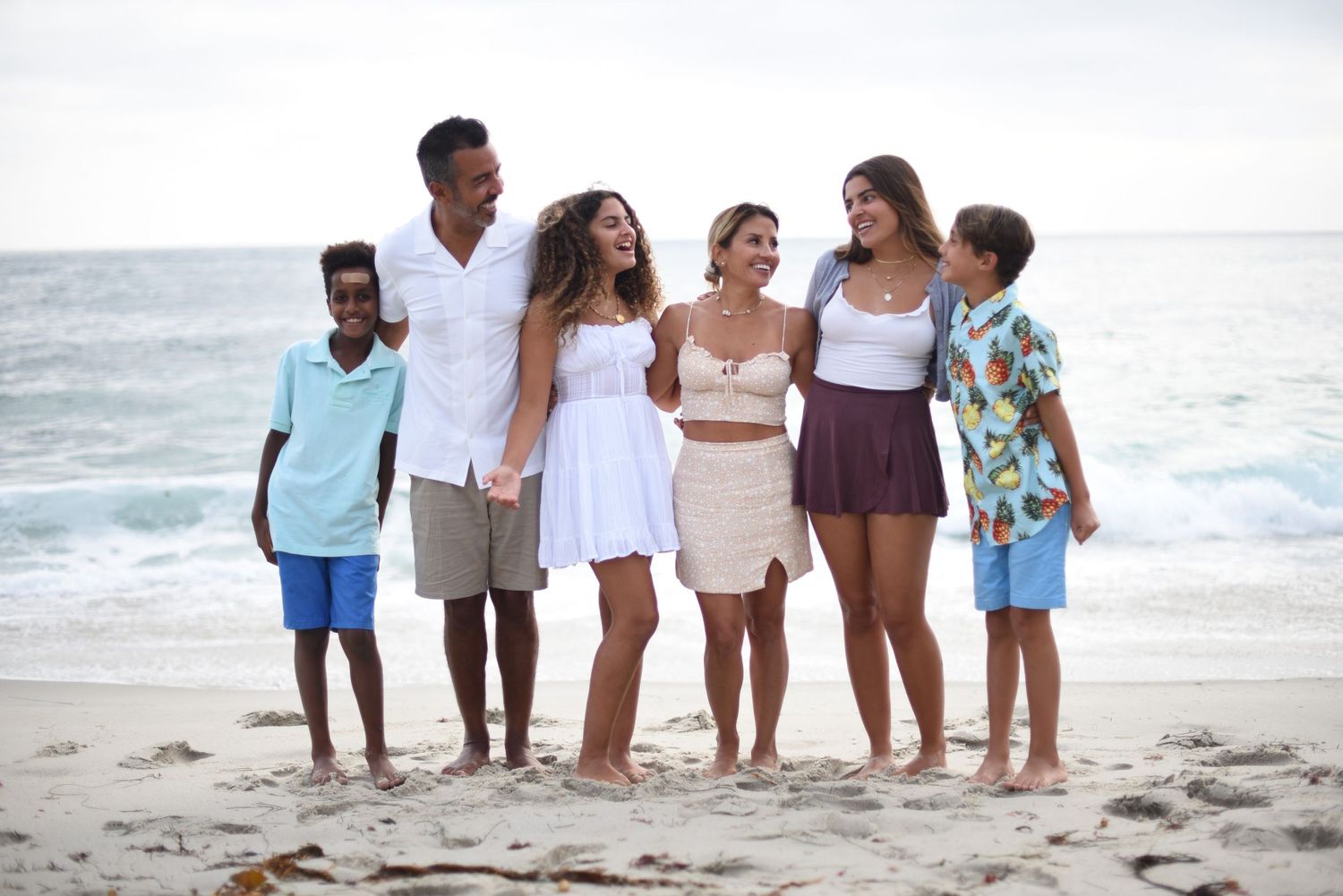 Extended family group photo at beach with ocean waves and coastal cliffs in background.