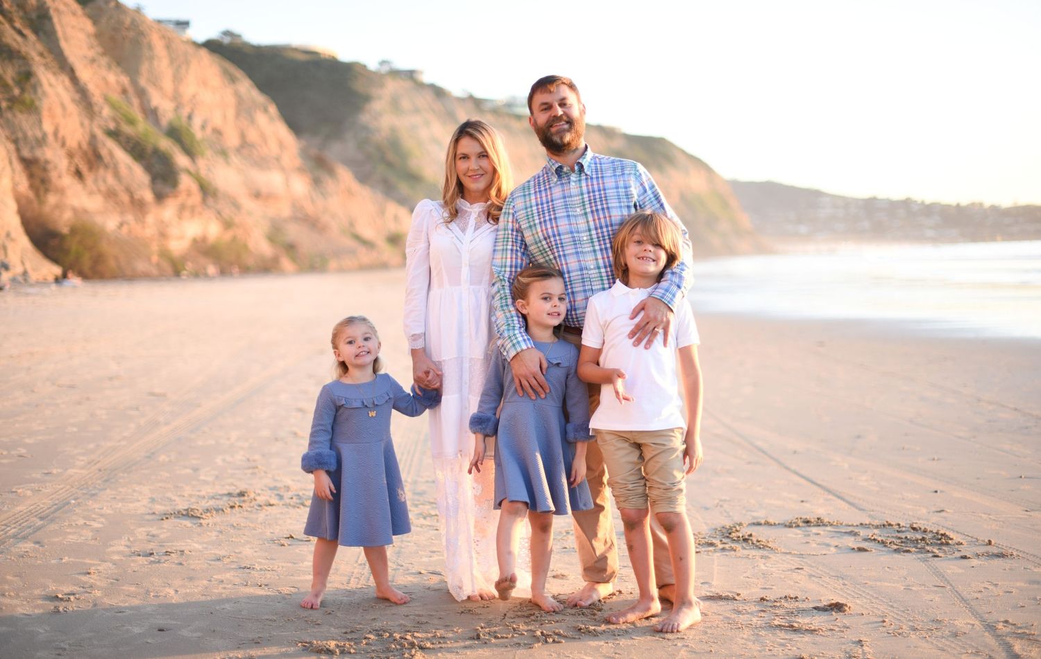 Family portrait session at sunset on beach with coordinated blue and white outfits.