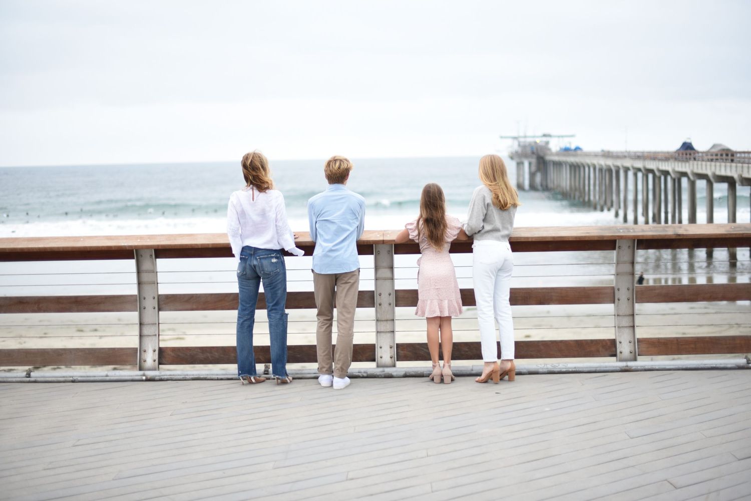 Family standing along wooden pier railing looking out at the ocean view.