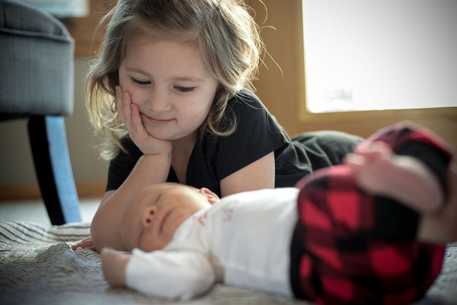 Big sisters laying on the floor with her new baby brother during their family's in-home newborn session in Sioux City.