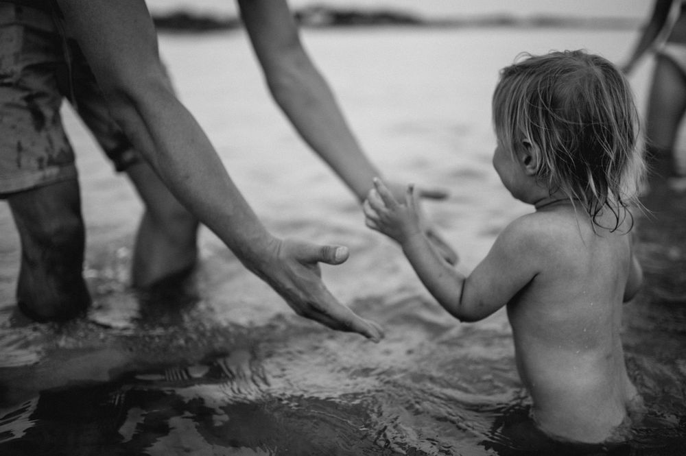 baby in the water walking towards her dad who is extending his warms towards her, Kent family photographer