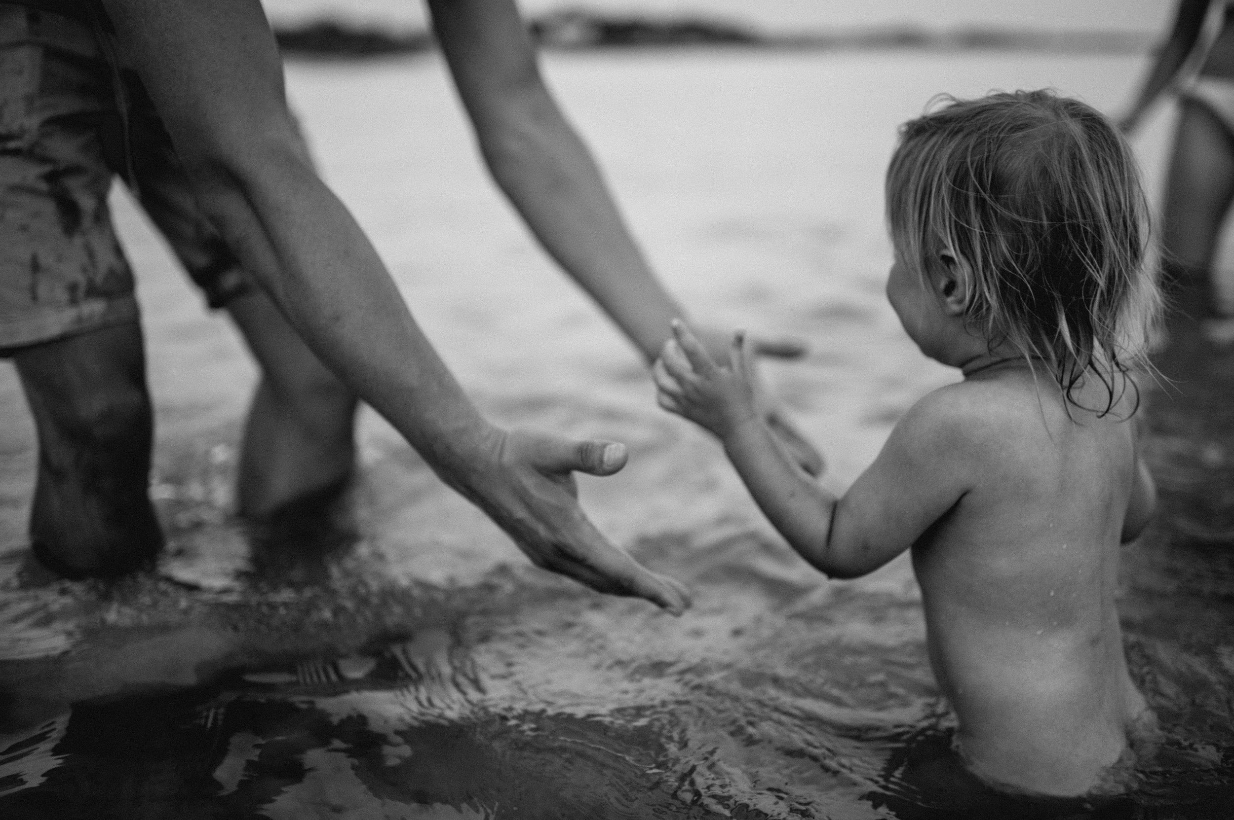 baby in the water walking towards her dad who is extending his warms towards her, Kent family photographer