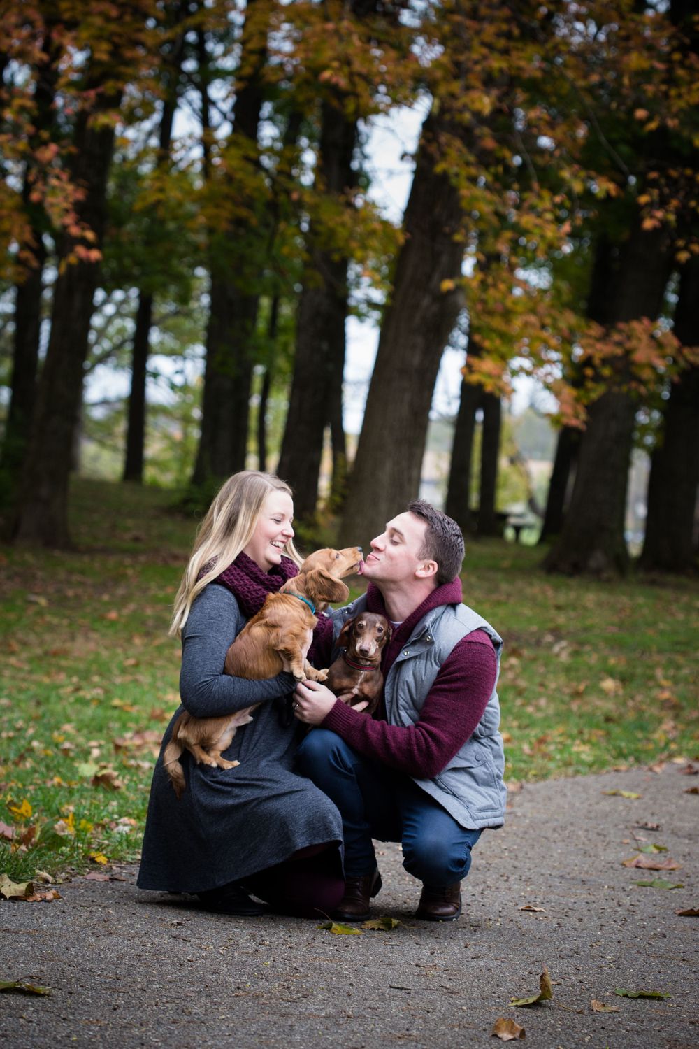 Playful fall engagement photos with couple and their dog on path covered in autumn leaves.