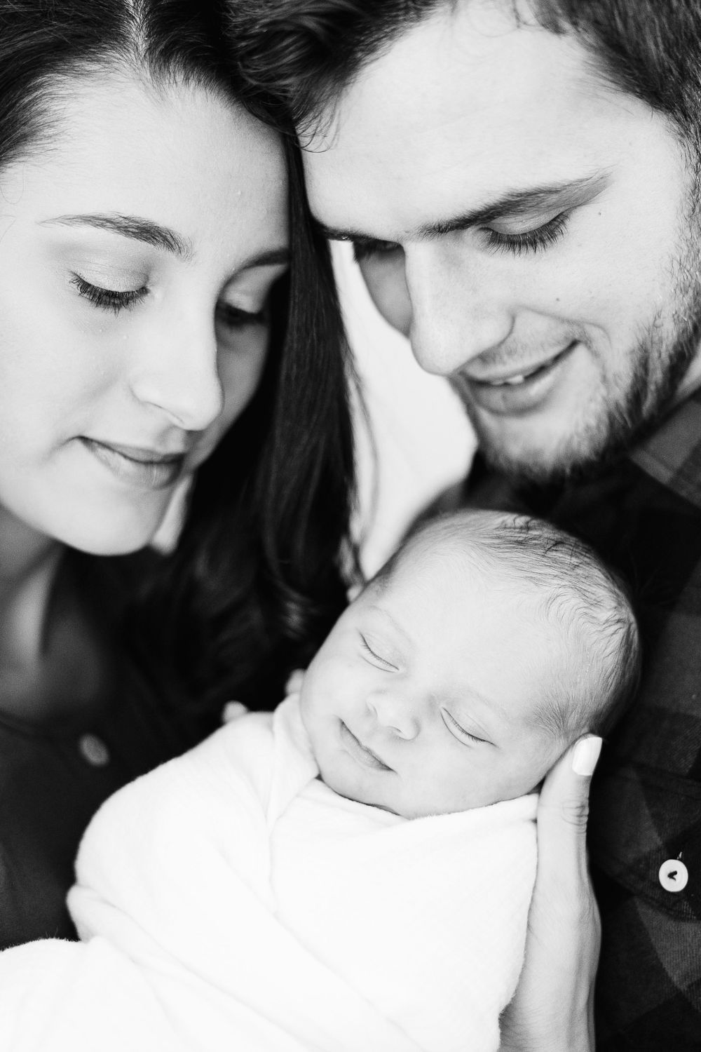 Black and white portrait of new parents with sleeping newborn baby.