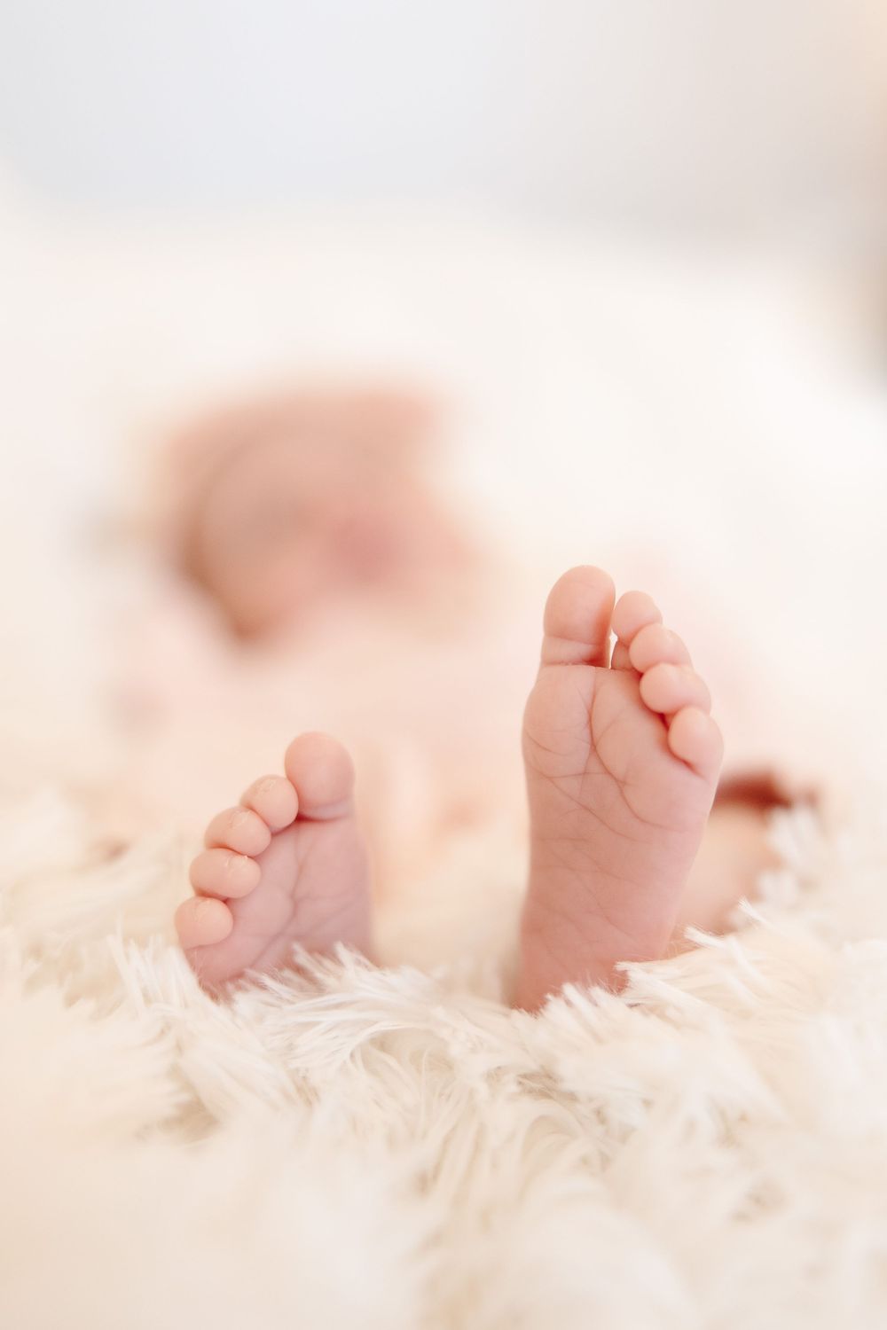 Close-up of tiny baby feet resting on soft white feathery fabric.