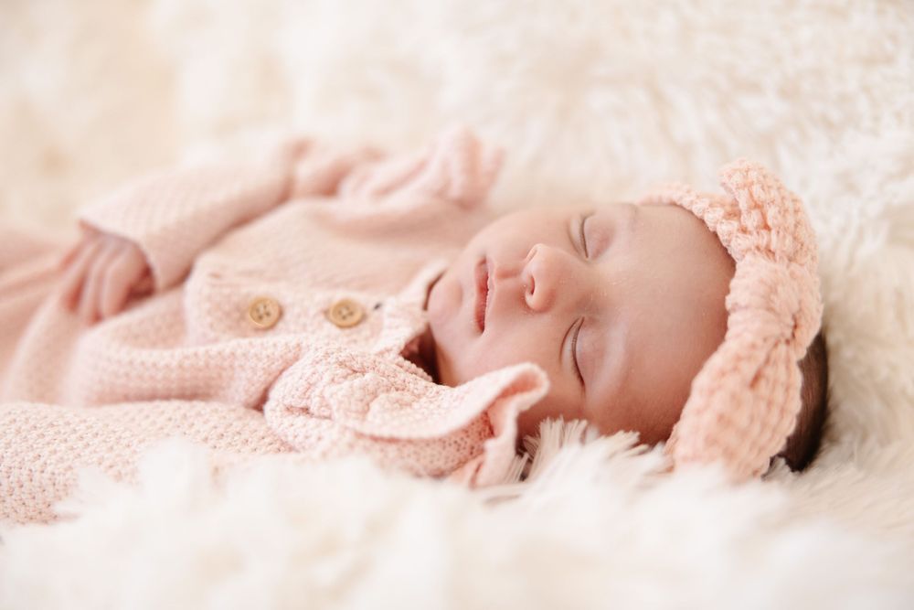Sleeping newborn baby in pink knit outfit on soft white blanket.