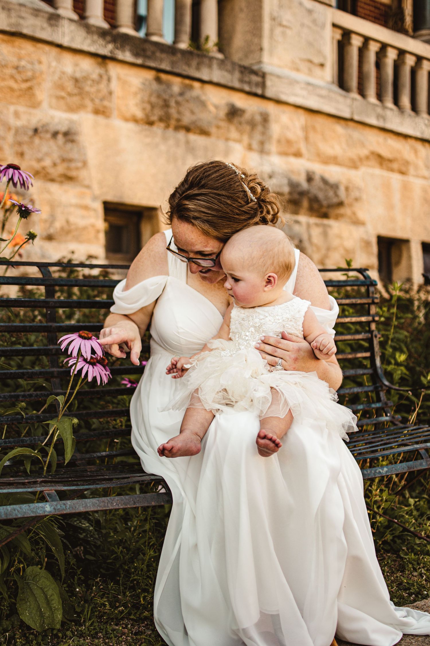 A tender moment captured between a mother and baby in white dresses near blooming purple flowers.