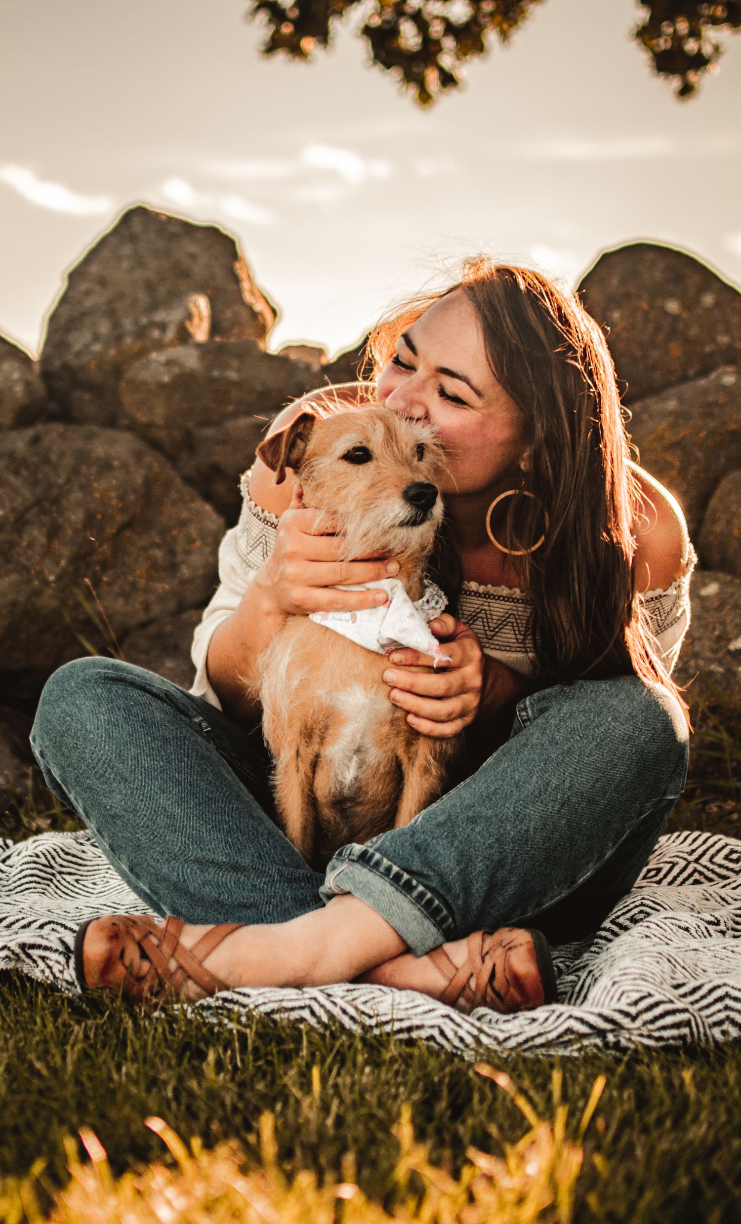 A sweet moment between a woman and her golden dog during golden hour on a blanket outdoors.