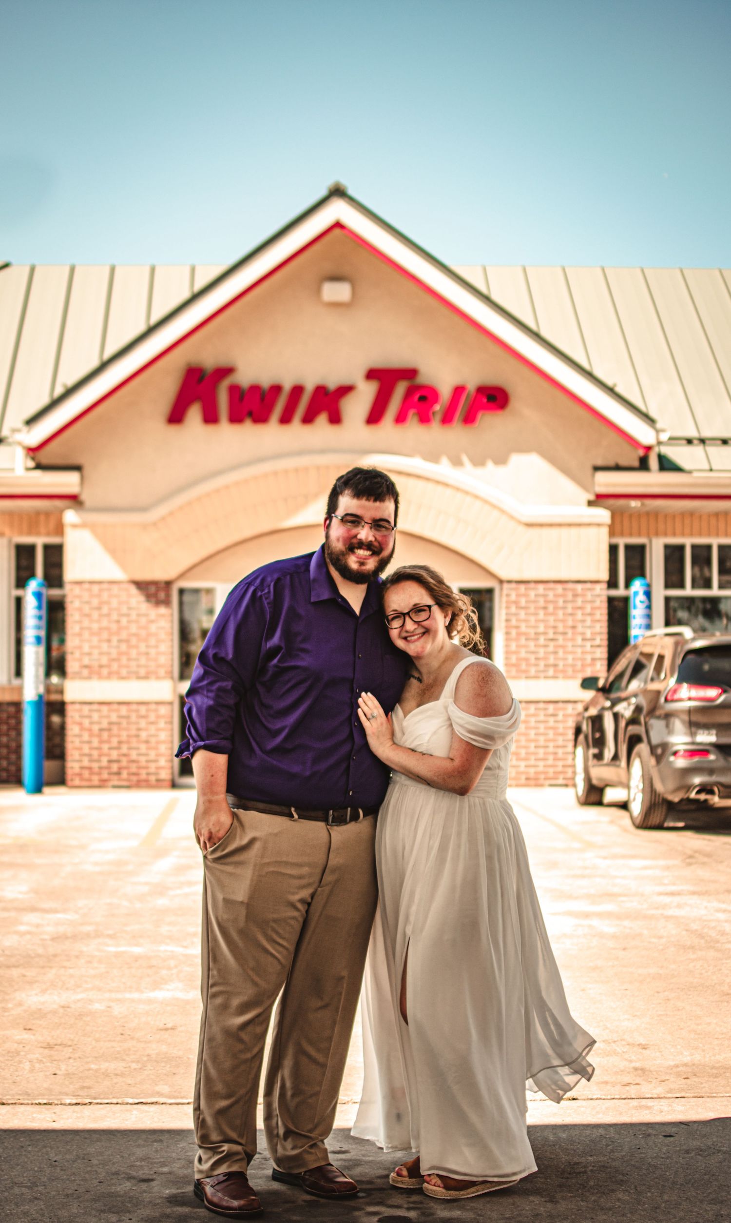 A couple in wedding attire poses in front of a Kwik Trip convenience store.