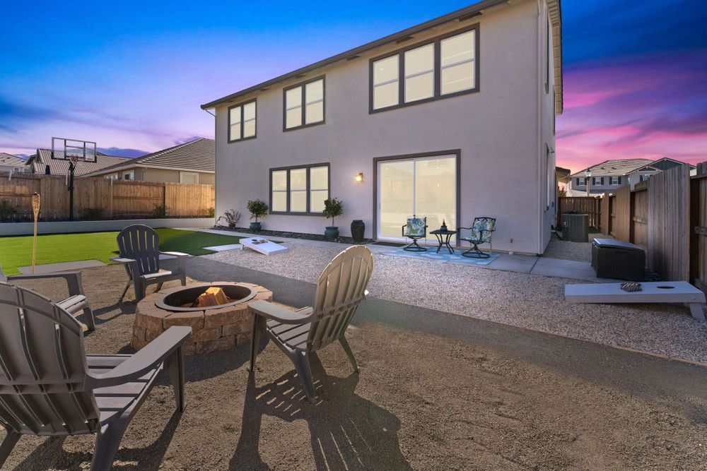 Backyard patio area with Adirondack chairs and fire pit at dusk.