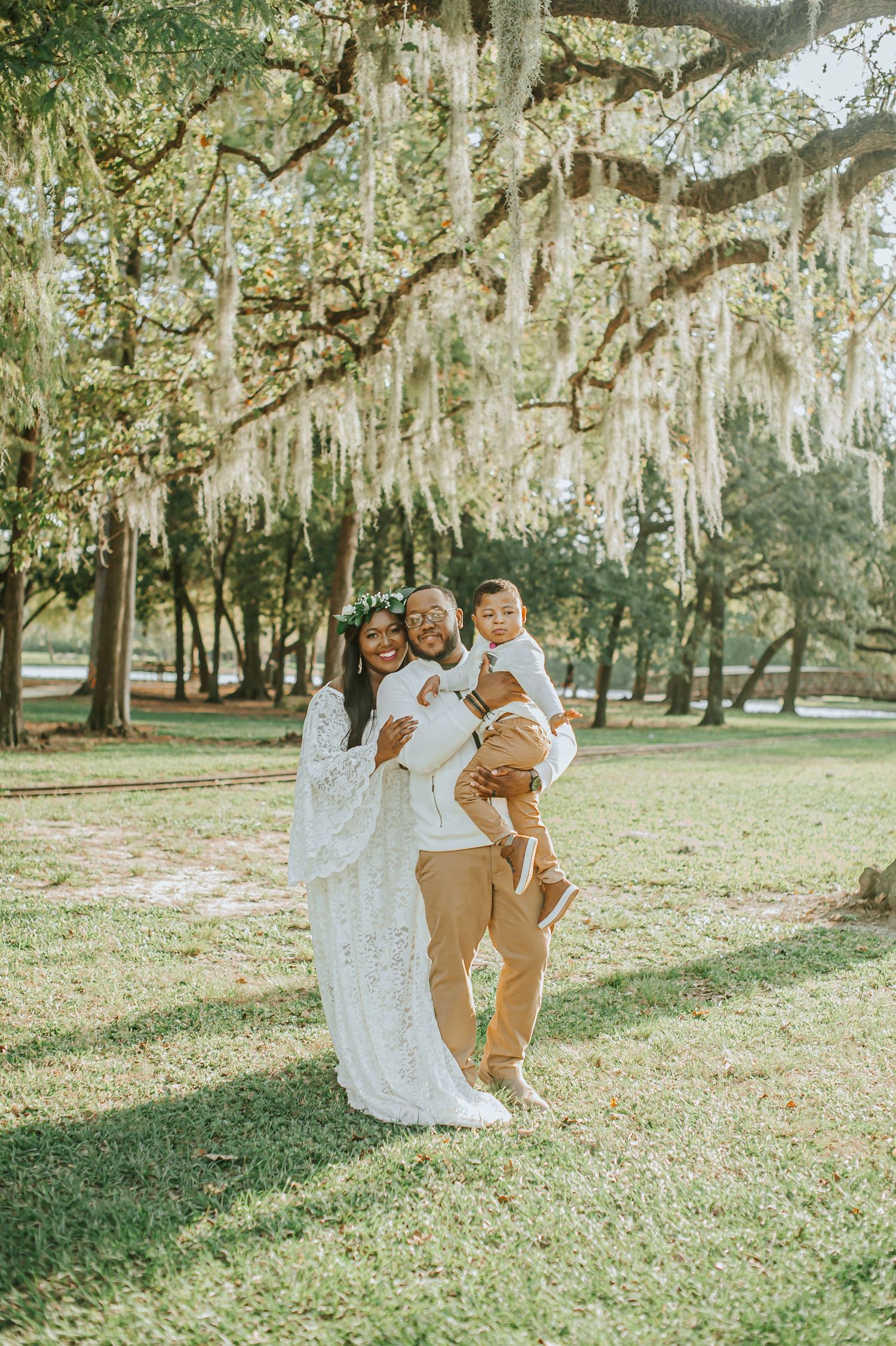 Family in white and tan outfits poses under Spanish moss-draped trees in a park setting.