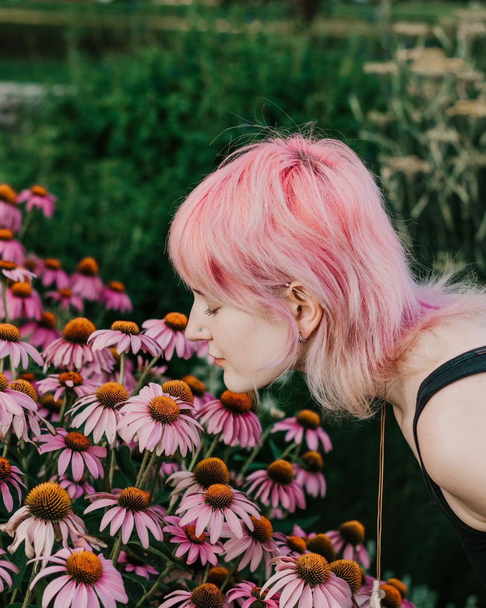 A young woman smells flowers nearly as pink as her hair