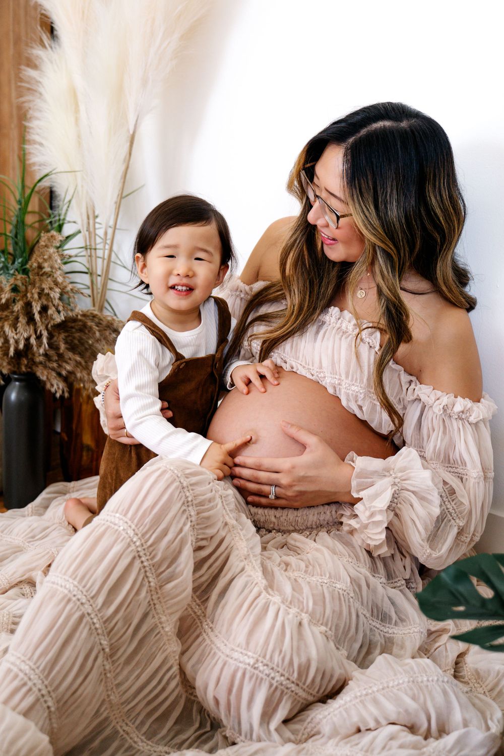 Heartwarming maternity photo with toddler touching pregnant belly against boho decor.