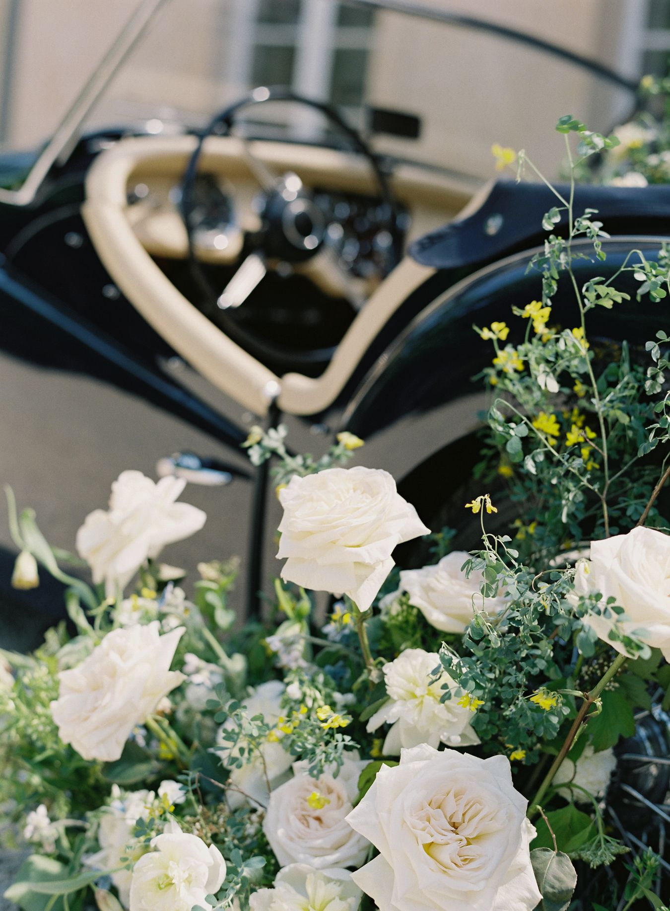 Elegant white roses and greenery adorn a vintage car with cream leather interior.