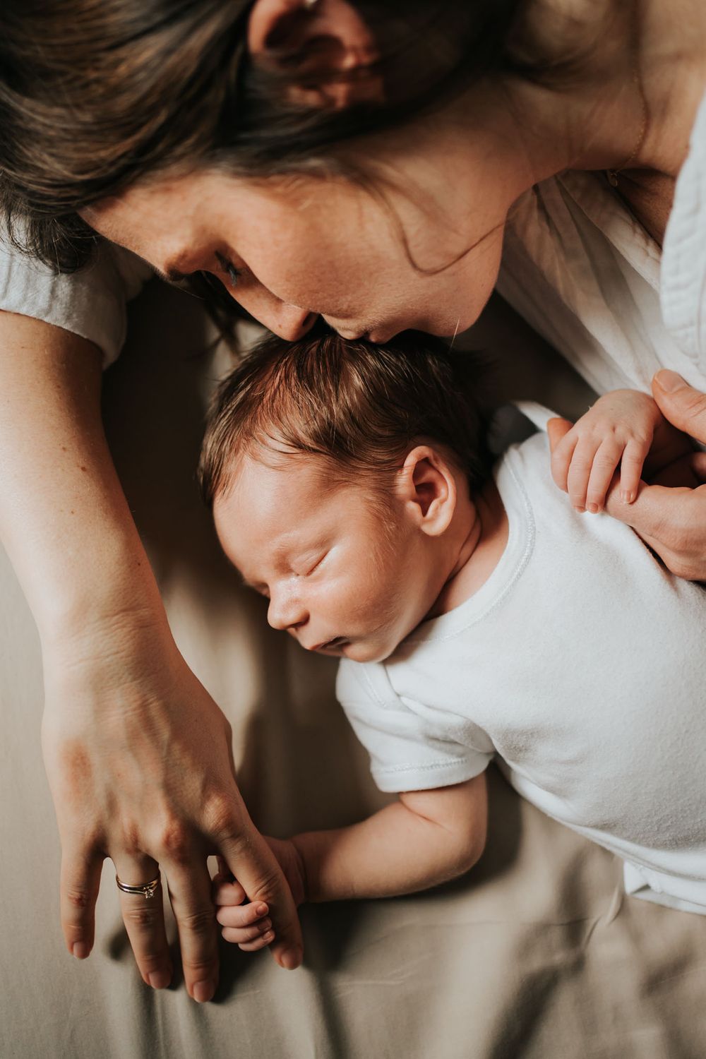 Mama czule i delikatnie całuje swojego małego synka, leżą razem na łóżku - domowa sesja noworodkowa Kraków