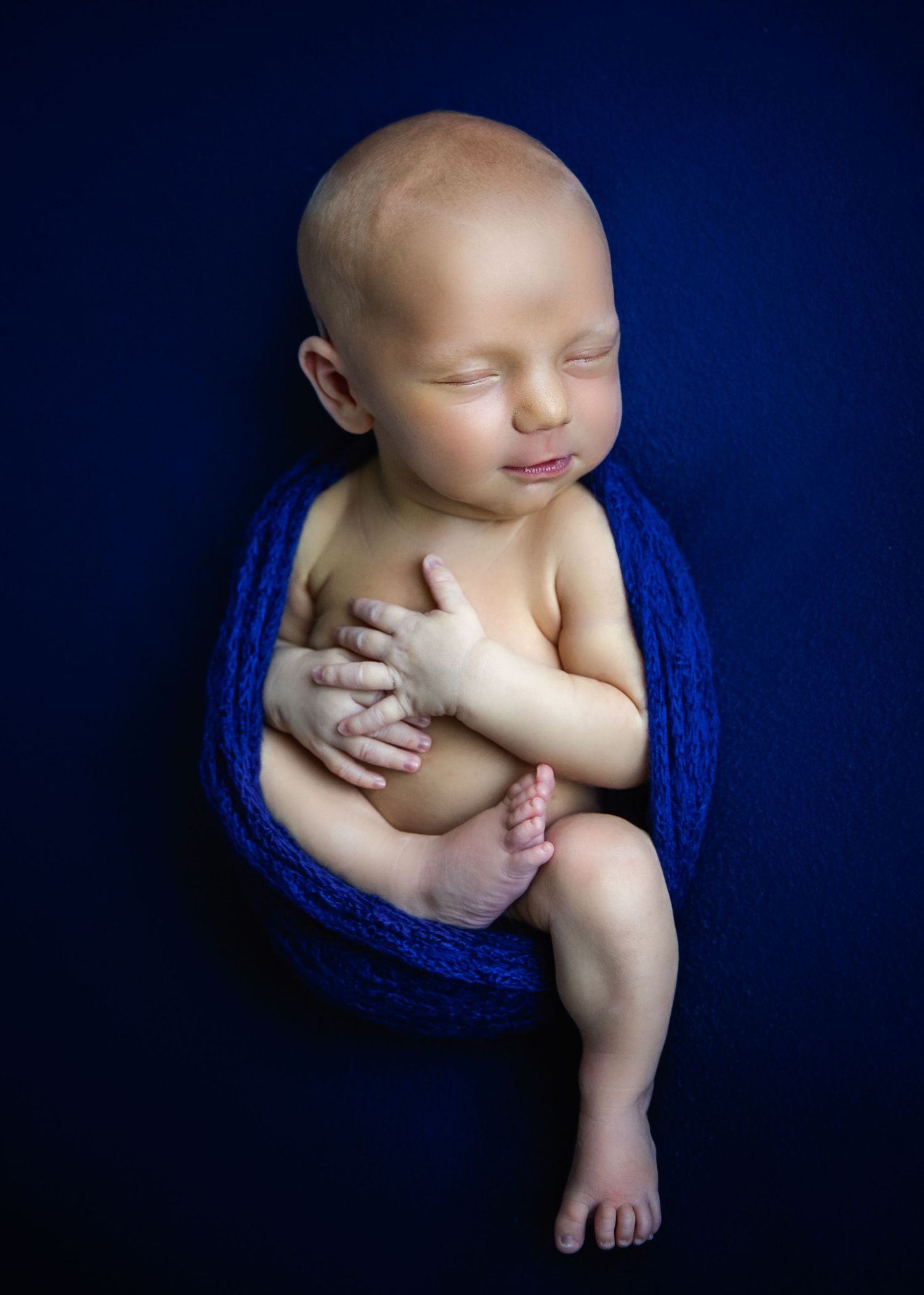 newborn baby boy with navy blue backdrop smiling for posed newborn photoshoot