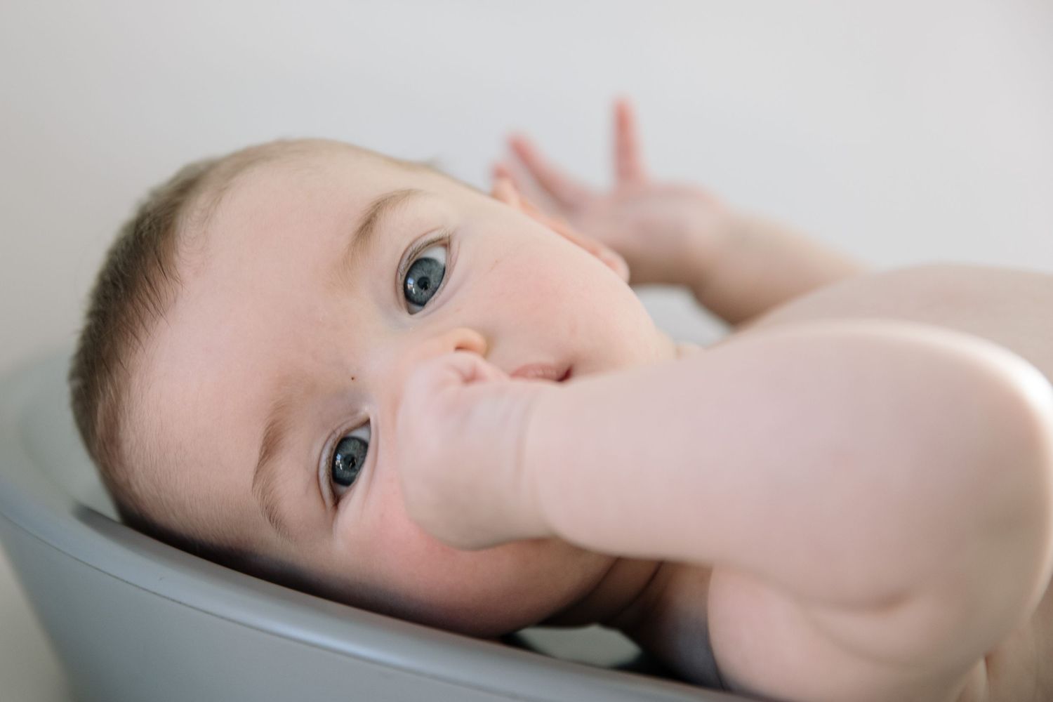 Baby lying on back with curious expression and fingers in mouth.