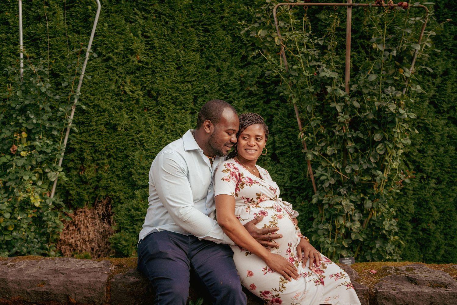 Expecting parents in floral outfits holding belly, intimate garden maternity session in the Rose Garden Portland.