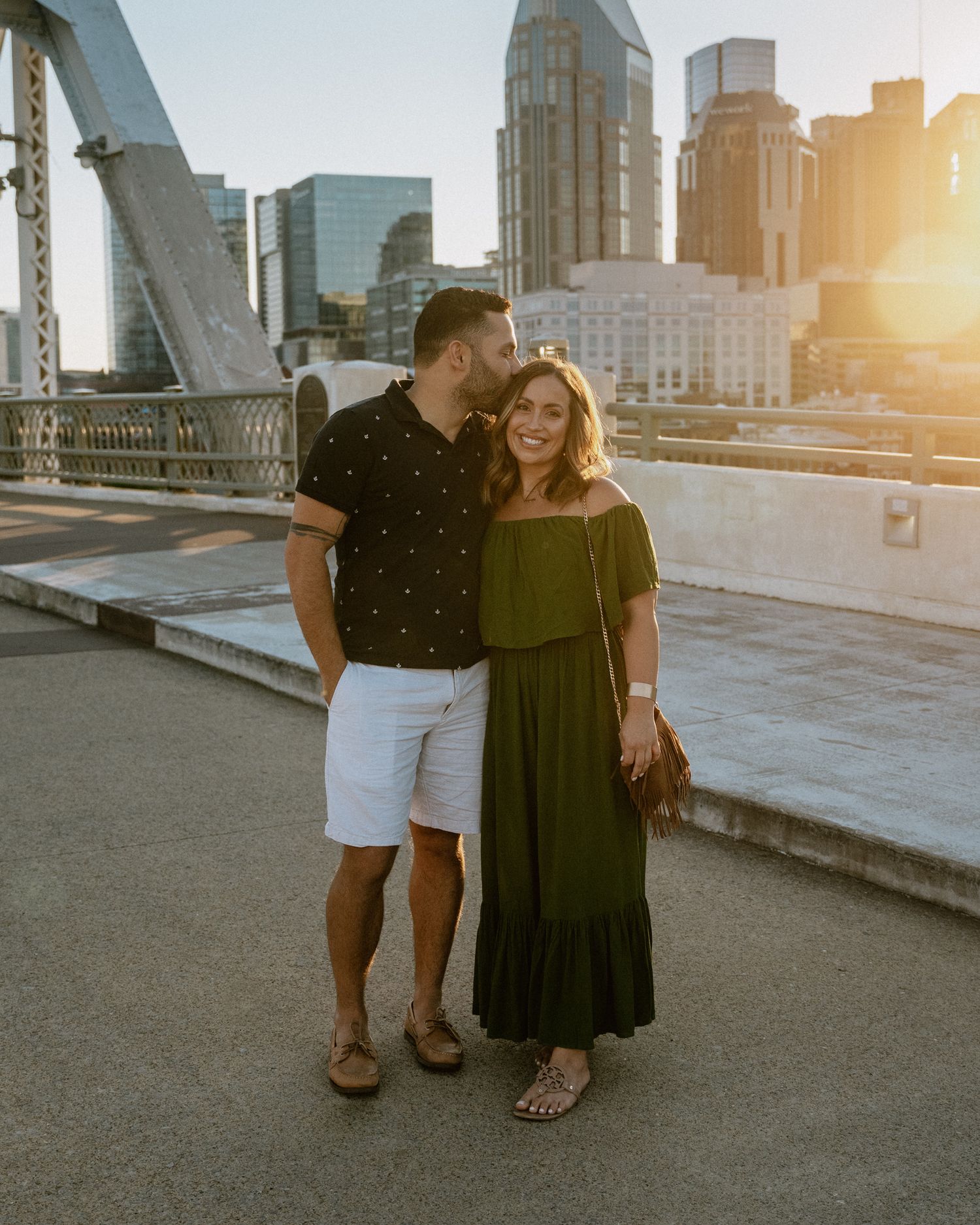 A couple embraces after a rooftop proposal with the city's golden sunset behind them.