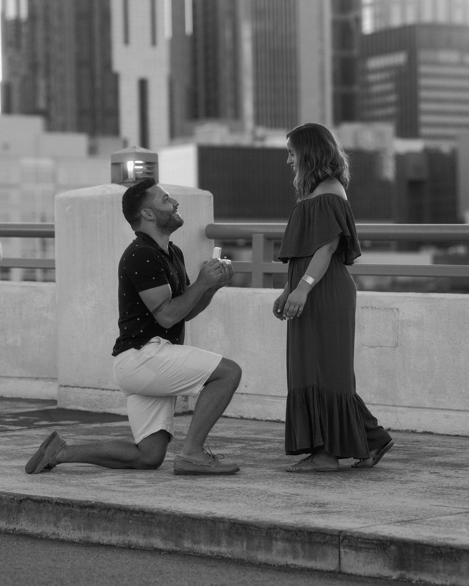 Black and white capture of a rooftop proposal against a city backdrop.