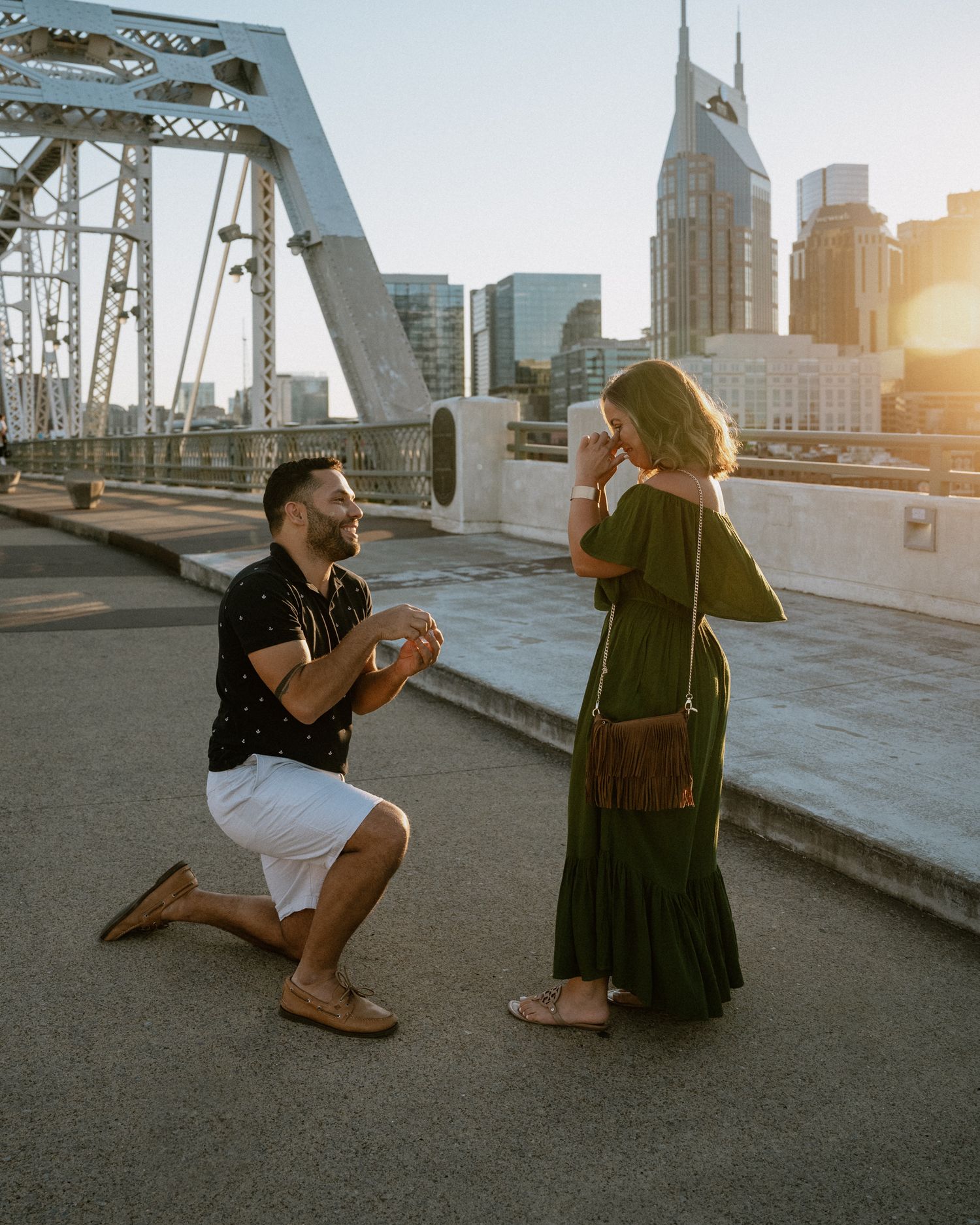 Two people share an emotional moment during a proposal on a Nashville bridge at golden hour.