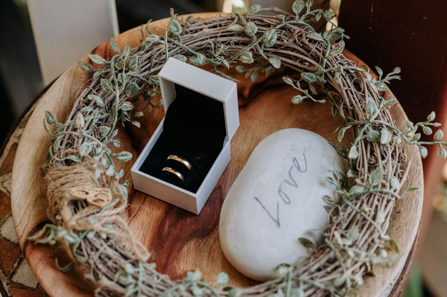 Wedding rings in black box placed on wooden surface with decorative wreath.