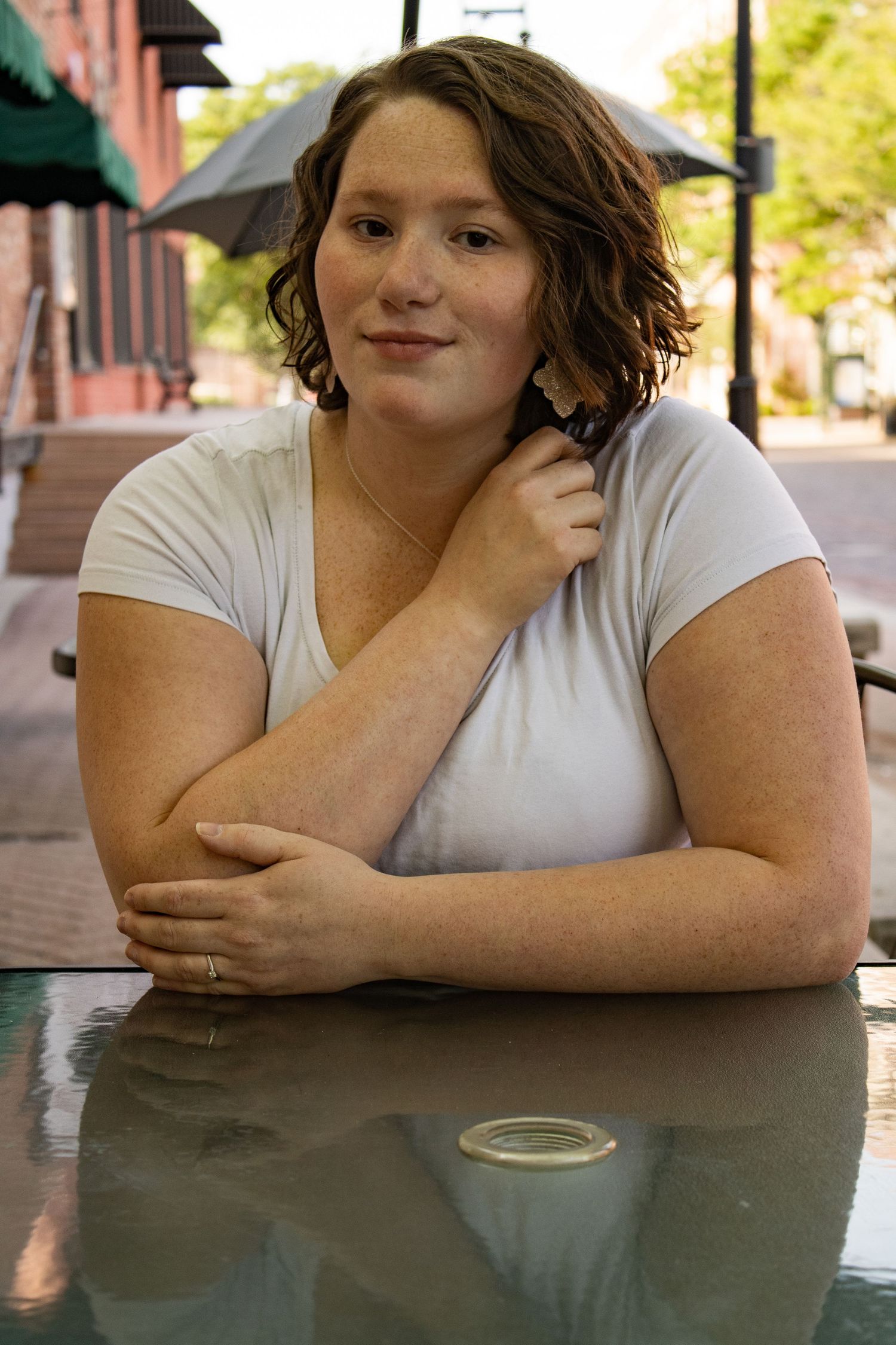 A person in a white t-shirt sits at a reflective table outdoors near a storefront.
