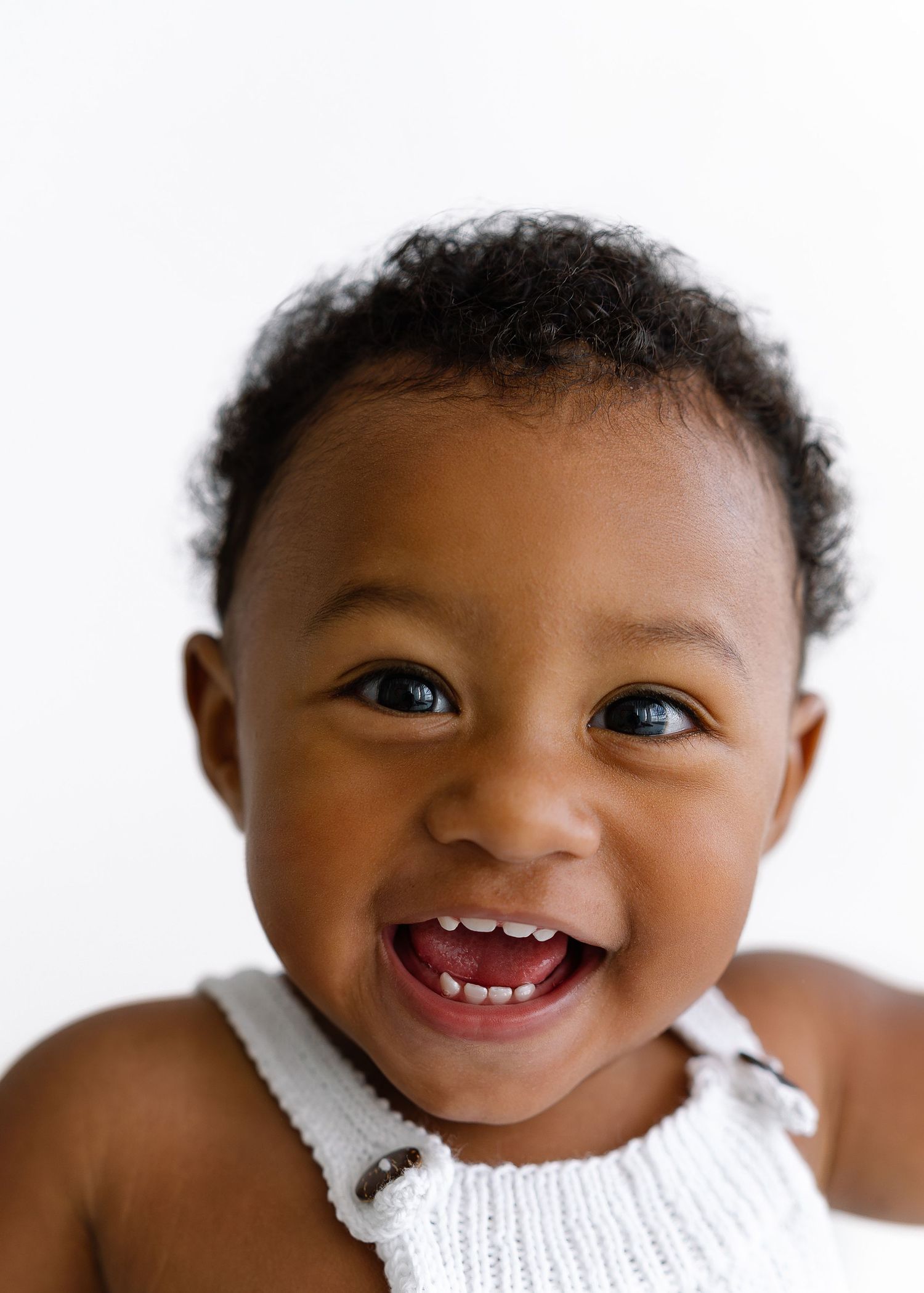Joyful toddler in white tank top smiling brightly against white background.
