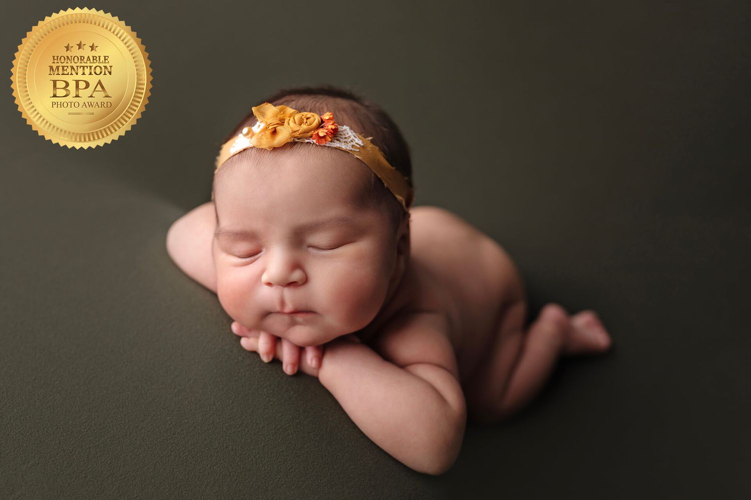 A peaceful newborn sleeping on a dark background wearing a delicate floral headband.