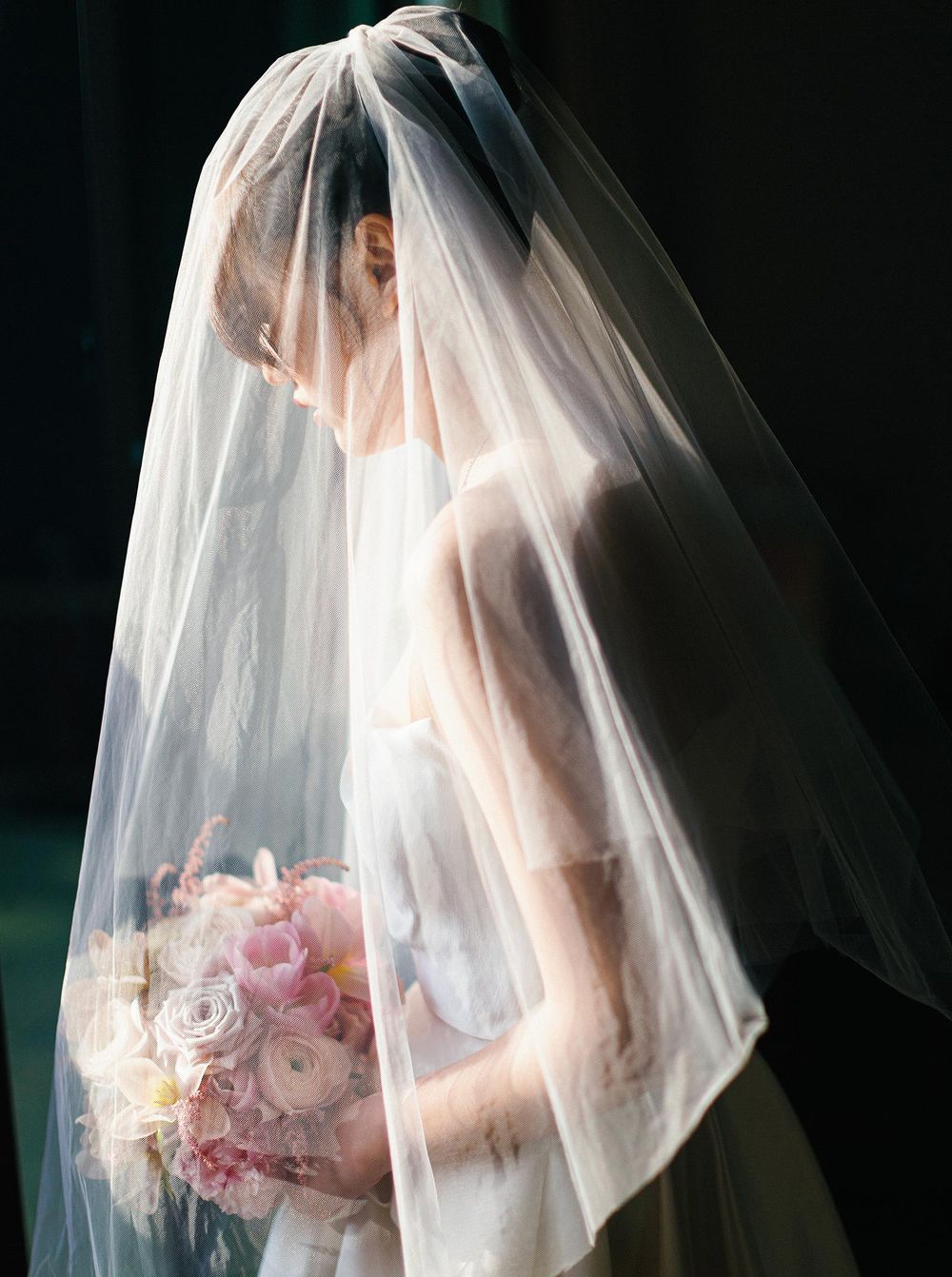 A bride in a wedding dress holding a bouquet, under a veil in Phuket, Thailand.
