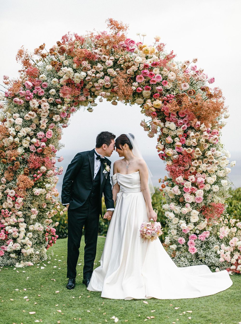 Wedding arch adorned with flowers, bride and groom celebrating under floral arch in Phuket, Thailand.