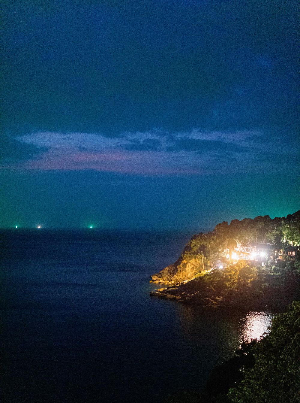 Nighttime in Phuket, Thailand: Ocean waves under a starry sky, with shore lights shining.