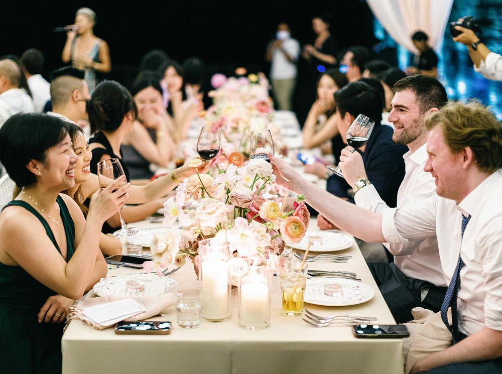 A group of people at a dinner table with wine glasses, enjoying a wedding reception in Phuket, Thailand.