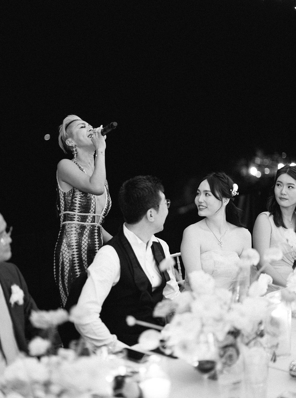 A bride and groom in a black and white photo at a wedding, with a singer performing for them at the reception in Phuket,