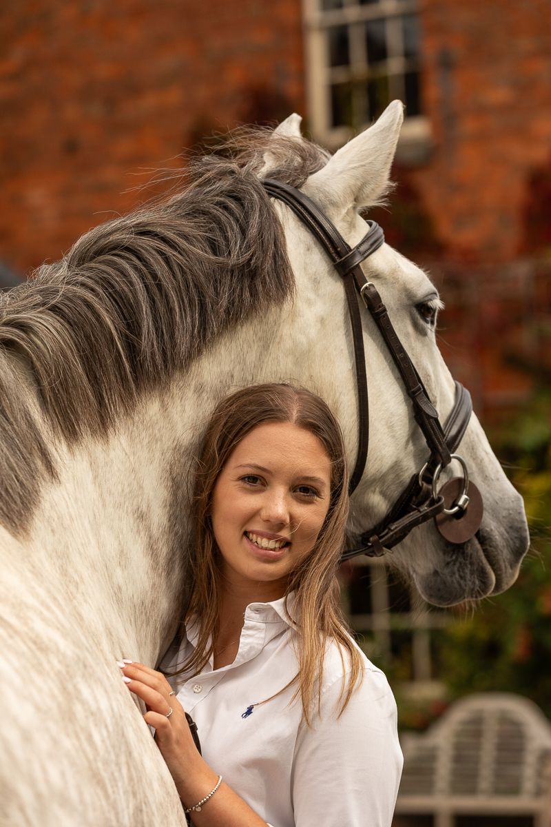 Beautiful grey horse with flowing mane poses against red brick building background.