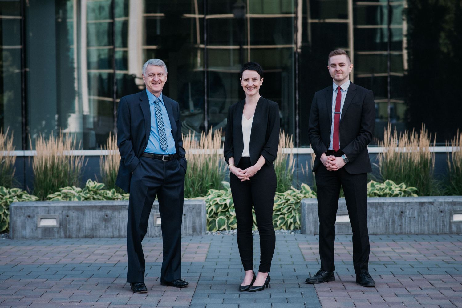 Professional business portrait of three people standing outside a modern building.