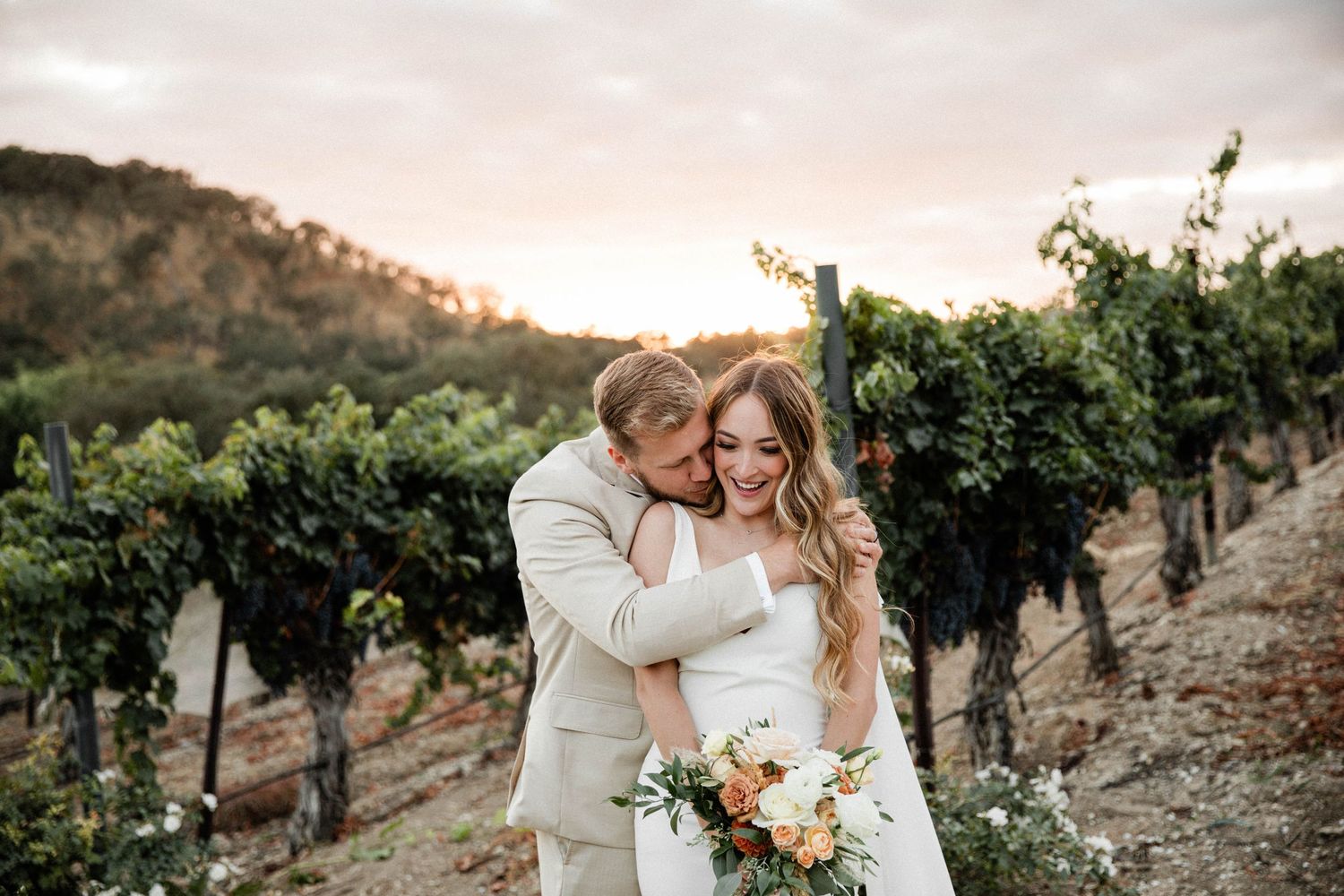 bride and groom embrace in front of the sunset after getting married in Paso Robles California at Cass Winery.