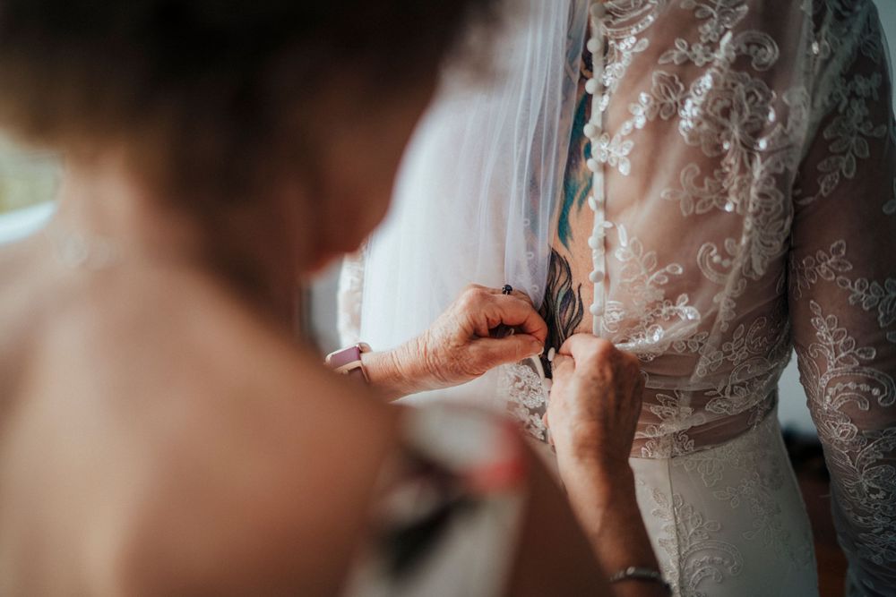 Close-up detail of hands fastening delicate buttons on an ornate lace wedding dress.