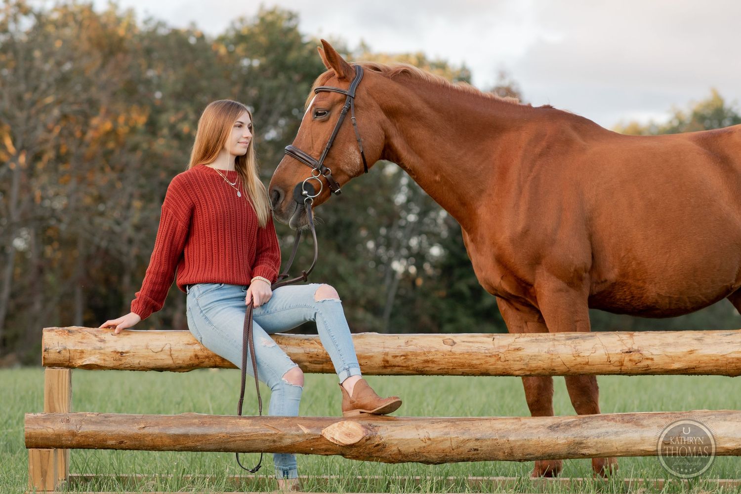 Horse and rider pose together on rustic wooden fence in autumn pasture.